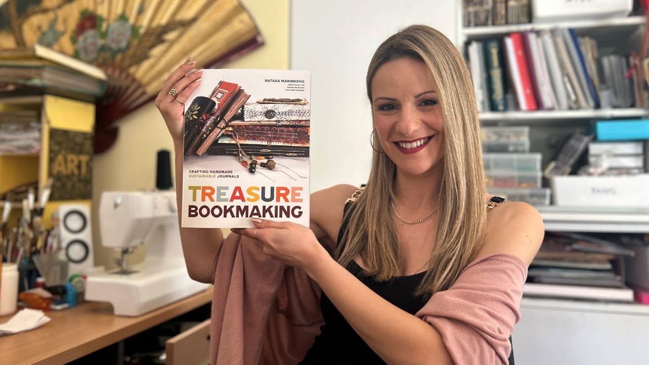 Natasa mid-laugh holding a finished treasure book, shelves of journals behind her